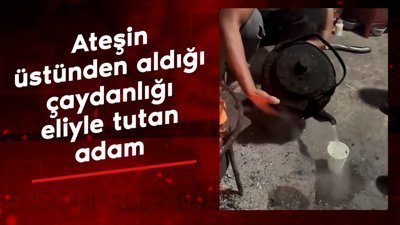 Ateşin üstünden aldığı çaydanlığı elleriyle tutan adam
